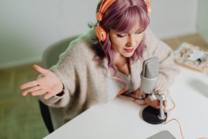 Woman sits at a desk speaking into a microphone. Featured image in a blog about podcast platforms.